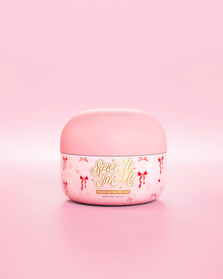 Pink tub of SLick It To Me shimmer melting body balm with decorative red bow elements on a pink background