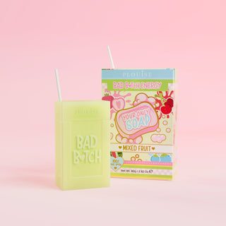 A green bar of soap with 'Bad Bitch' engraved on it, accompanied by a colourful juice box package with 'Mixed Fruit' labelled on it, presented on a pink background.