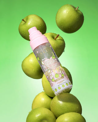 Bottle of P. Louise Sweet Spritz Apple Hydrating Face Mist surrounded by green apples on a green background